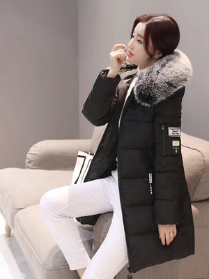 Woman wearing a black winter coat with fur hood sitting on a couch.