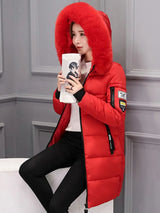 Person wearing a red puffer jacket with a fur-lined hood, sitting against a gray wall.