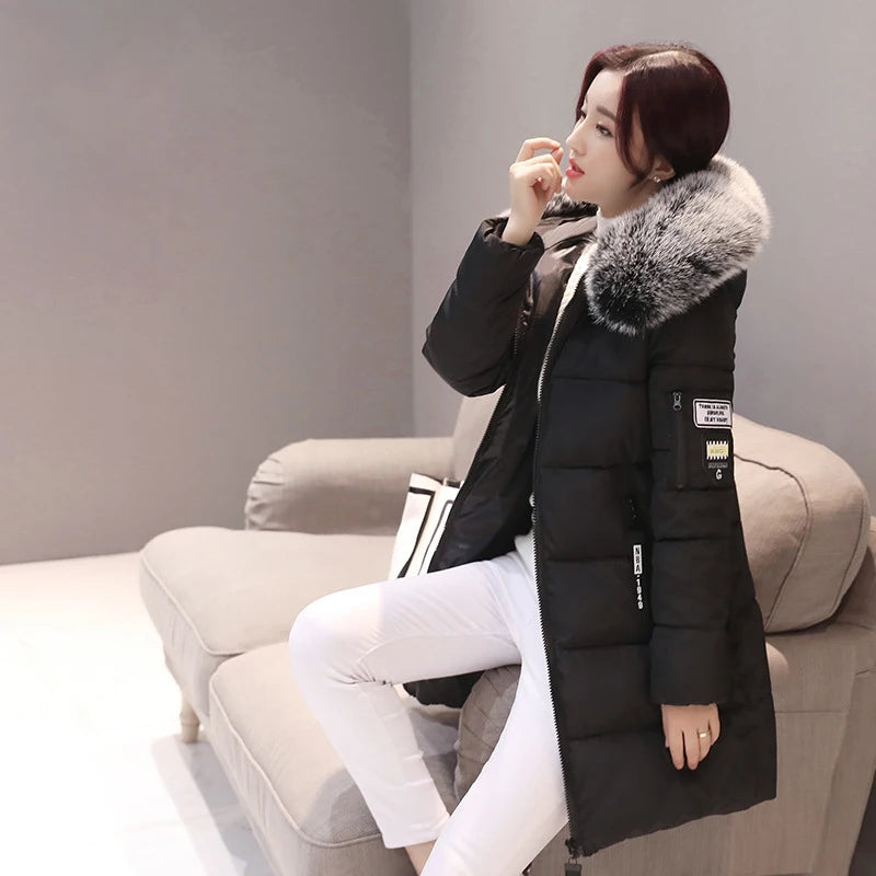Woman wearing a black puffer jacket with fur collar sitting on a beige sofa.