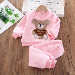 Pink children's outfit with teddy bear design on a wooden surface