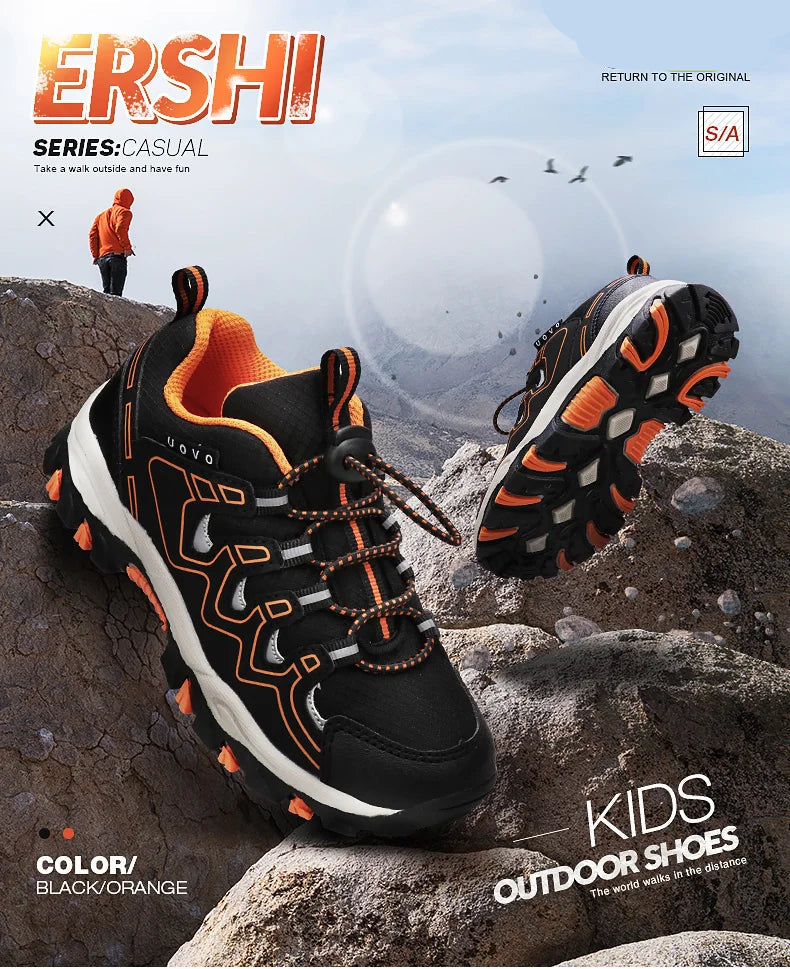 Black and orange kids' outdoor shoes on rocks with branding.