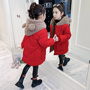 Child wearing a red coat with a fur-lined hood, standing in front of a mirror.