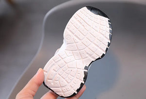 Close-up of a white and black sneaker sole held by a hand against a neutral background