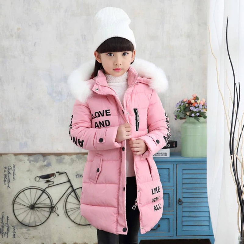 Child wearing a pink winter coat with fur-lined hood in a room setting.