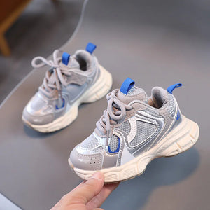 Gray and blue children's sneakers held by a hand on a gray surface