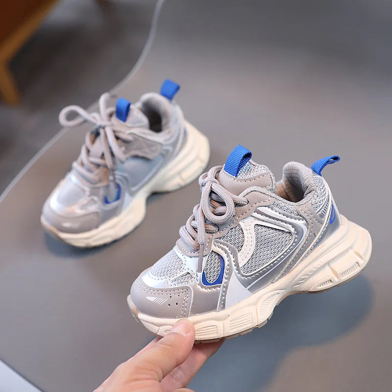 Gray and blue children's sneakers held by a hand on a gray surface