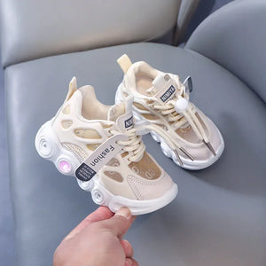 Beige children's sneakers with white soles held by a hand on a gray surface.