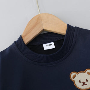 Navy blue sweater with a teddy bear design on a wooden hanger against a light gray background