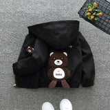Black hooded jacket with a teddy bear plush toy on a gray floor.