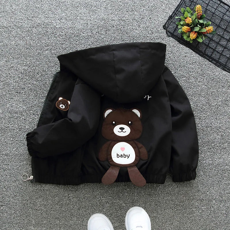 Black hooded jacket with a teddy bear plush toy on a gray floor.
