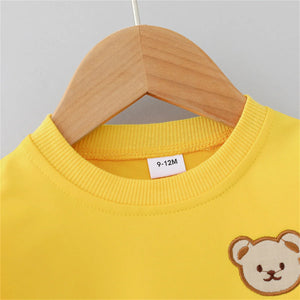 Yellow children's sweatshirt with a bear patch on a wooden hanger against a gray background