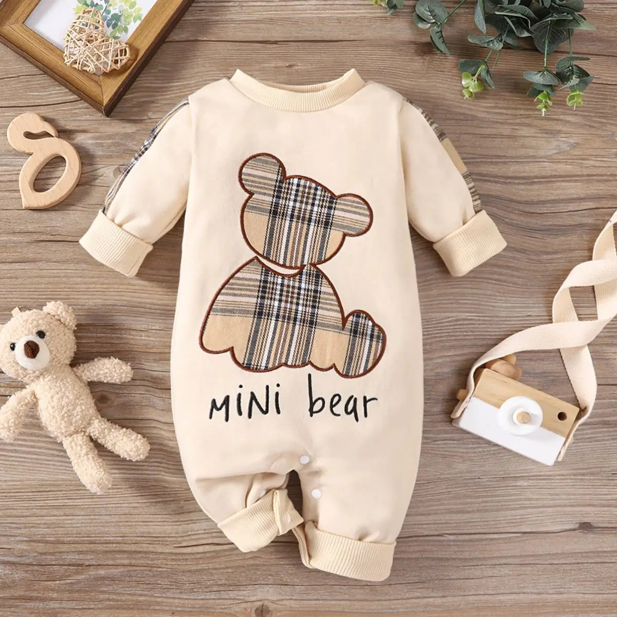 Baby romper with plaid bear design and 'mini bear' text on a wooden surface.