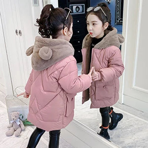 Two children in pink winter coats standing in front of a mirror.