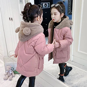 Two children in pink winter coats standing in front of a mirror.