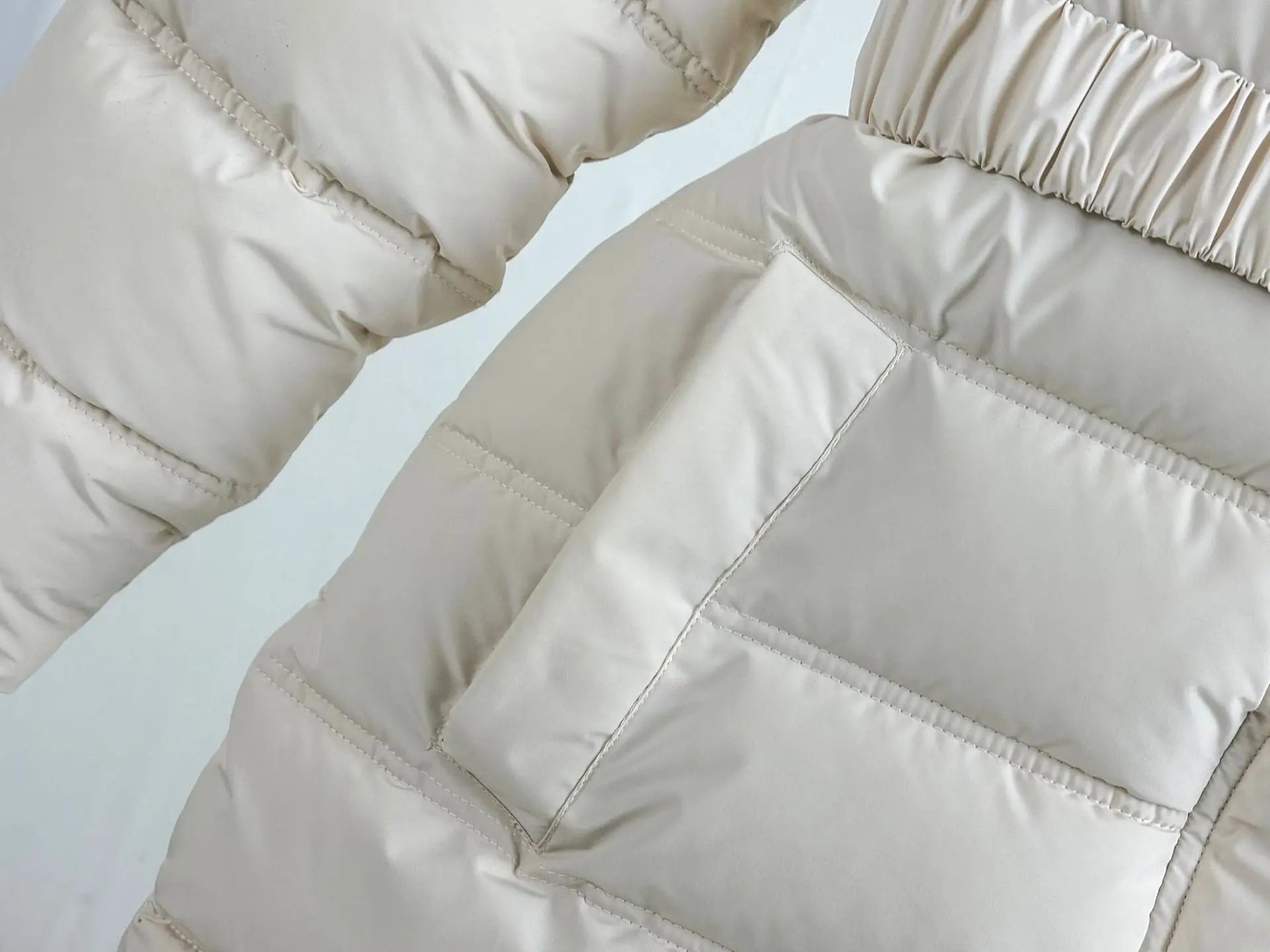 Close-up of a beige puffer jacket with quilted pattern on a light gray background