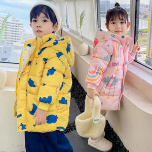 Two children wearing colorful winter jackets by a window with a cityscape view.
