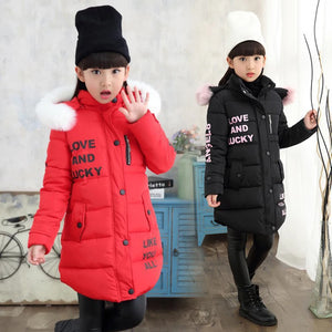 Two children wearing winter jackets with fur-lined hoods in a room setting.