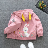 Pink children's jacket with bunny design on a gray floor.