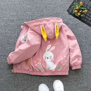 Pink children's jacket with bunny design on a gray floor.