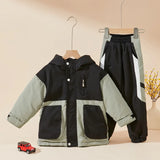 Children's jacket and pants set on hangers with a small toy car on a beige surface.
