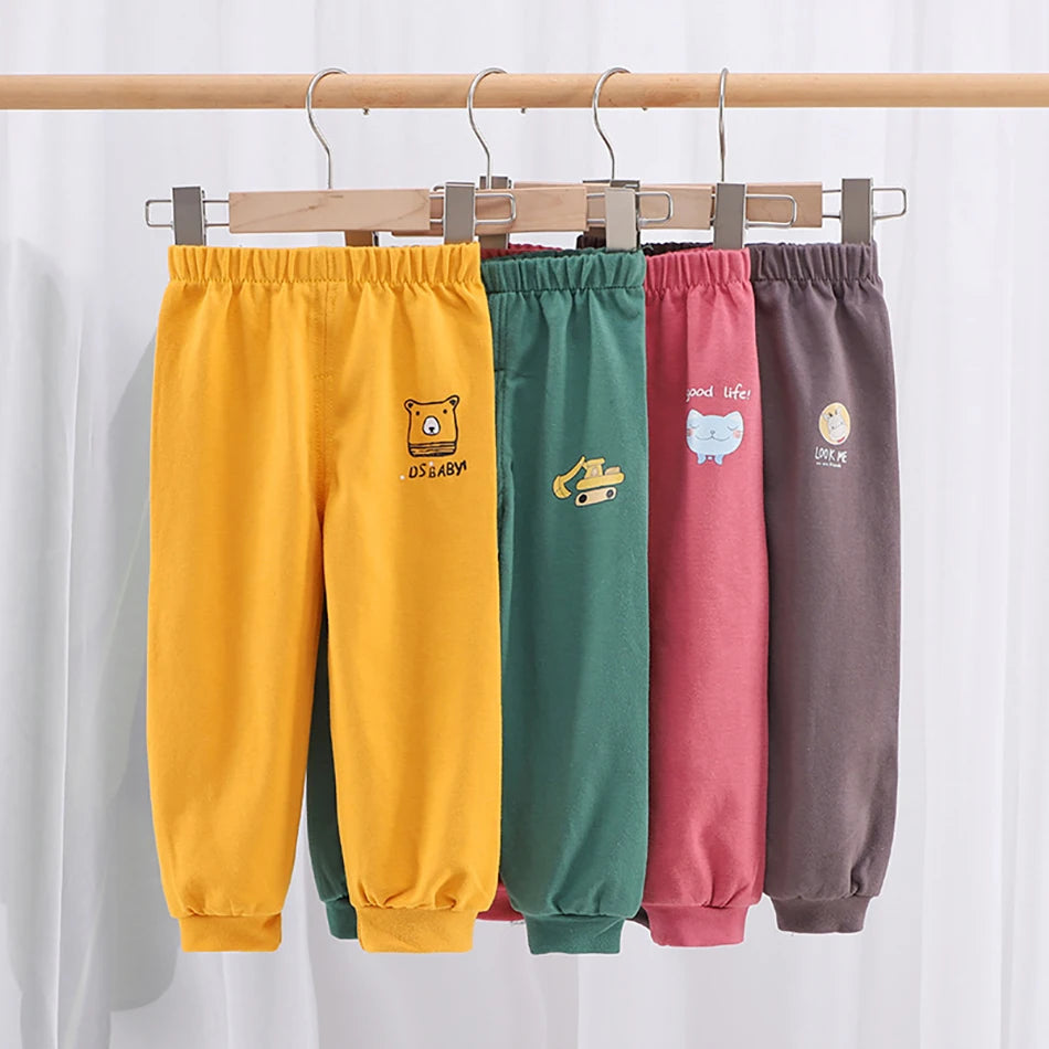 Four pairs of colorful children's sweatpants hanging on a rack against a white background.
