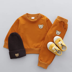 Children's orange sweatshirt, black beanie, and yellow shoes with bear designs on a gray background