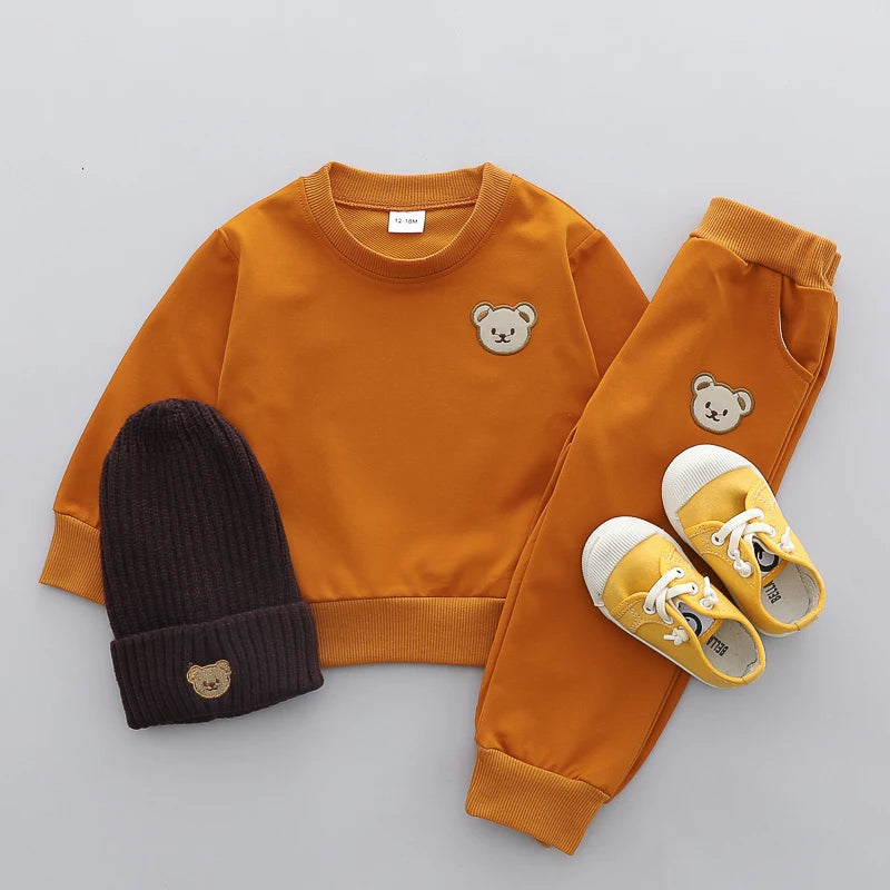 Children's orange sweatshirt, black beanie, and yellow shoes with bear designs on a gray background
