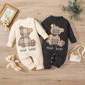 Two baby rompers with teddy bear designs on a wooden surface.