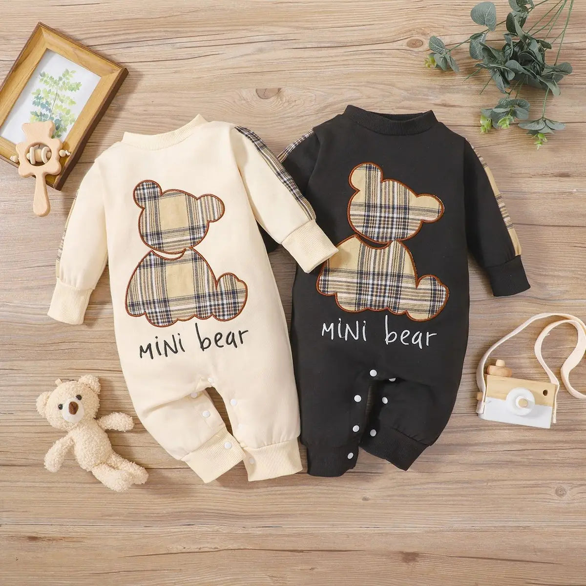 Two baby rompers with teddy bear designs on a wooden surface.