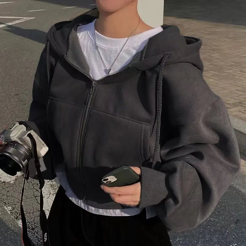Person wearing a black hoodie holding a phone and camera on a street.