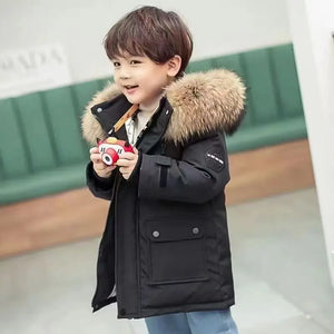 Child wearing a black coat with a fur-lined hood, holding a toy, against a blurred indoor background.