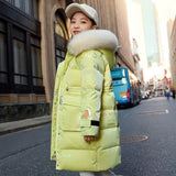 Person wearing a long yellow puffer coat with a fur-lined hood on a city street.