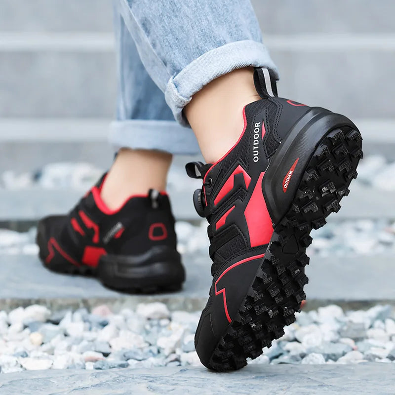 Black and red outdoor shoes worn on a person's foot, standing on a stone surface.