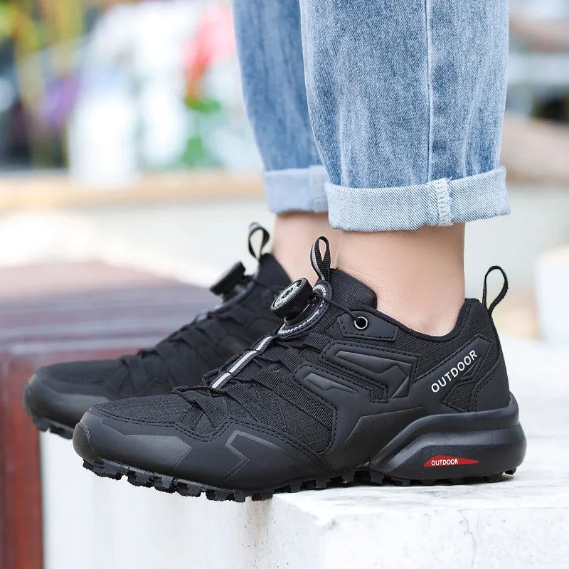Black outdoor shoes worn with rolled-up jeans on a blurred background