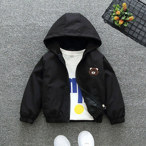 Black hooded jacket with a bear patch on a gray surface