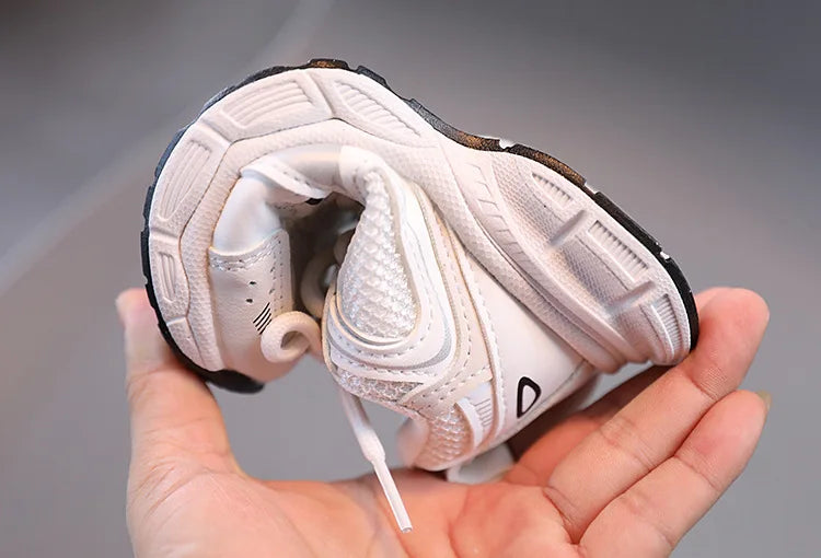 White sneaker with black accents held in a hand against a gray background