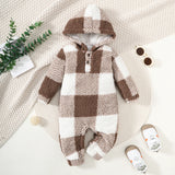 Plaid baby onesie with a hood on a textured surface with shoes and a plant.