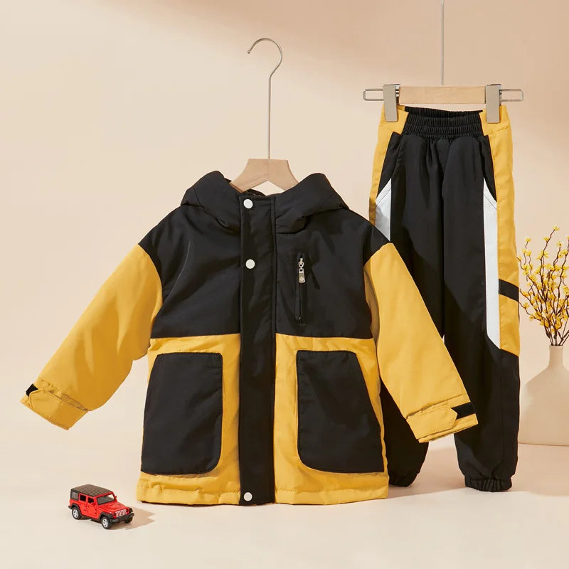 Black and yellow jacket and pants set on hangers with a small red car in front on a beige background.