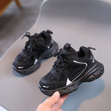 Black children's sneakers on a gray surface with a hand holding one shoe.