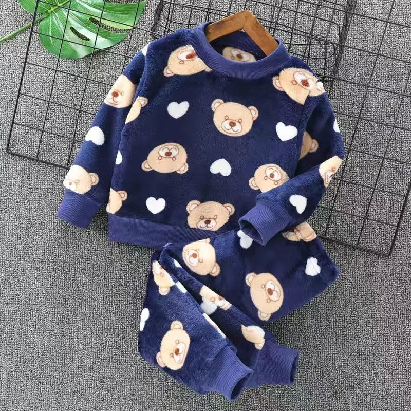 Children's navy blue pajama set with teddy bear and heart patterns on a gray surface.