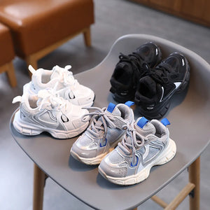 Four pairs of children's sneakers in white, gray, and black on a chair.