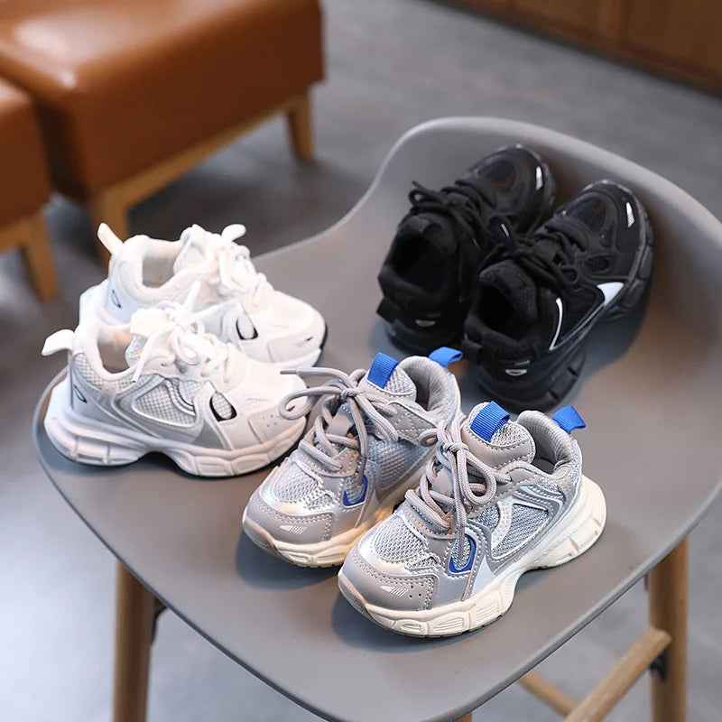 Four pairs of children's sneakers in white, gray, and black on a chair.