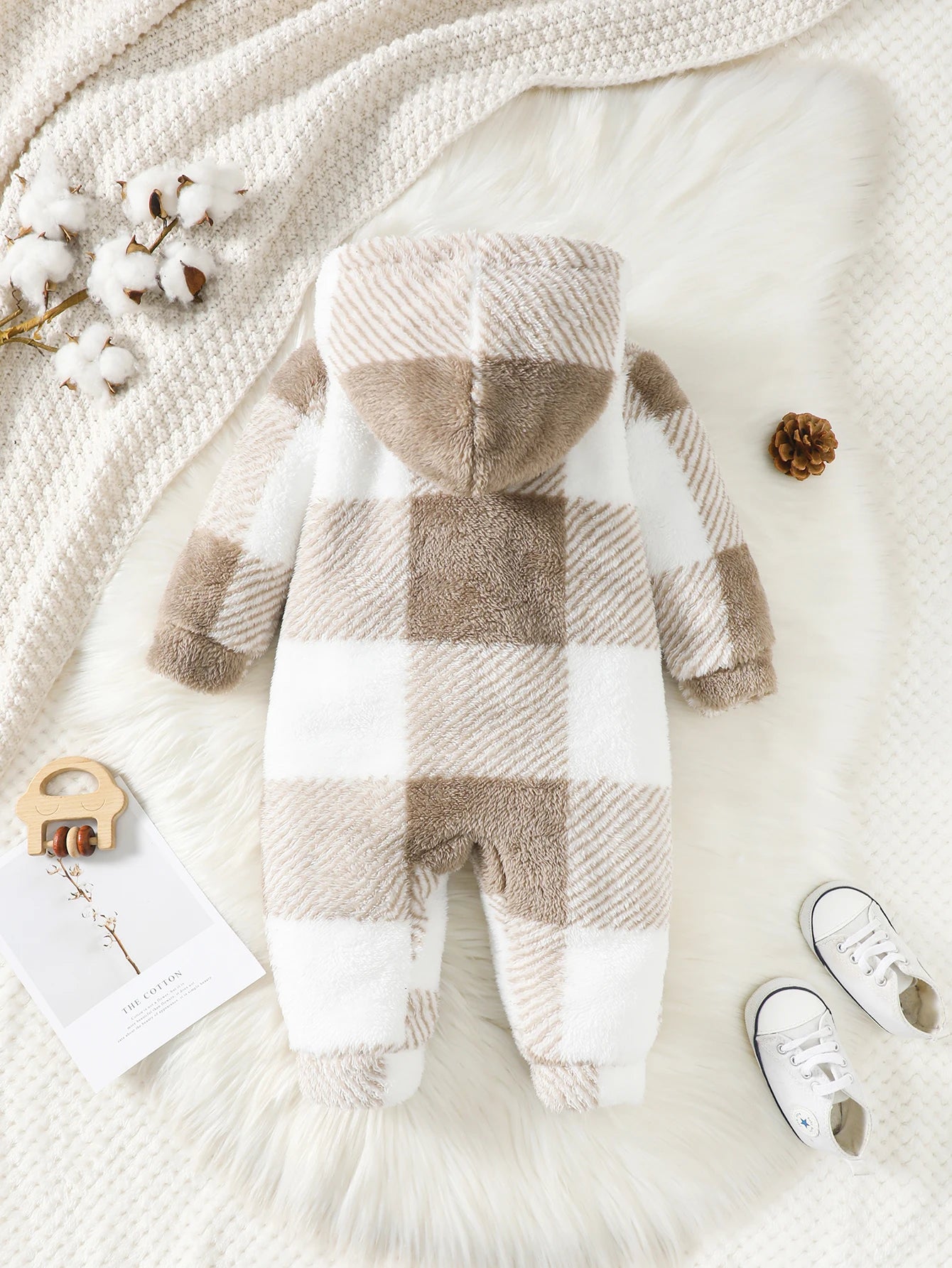Plaid baby romper on a soft white surface with decorative elements.