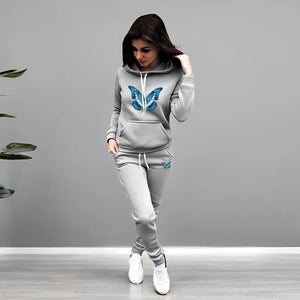 Woman wearing a gray tracksuit with butterfly designs on a plain background