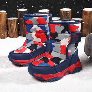 Camouflage-patterned children's boots in red, blue, and gray on a snowy background.