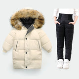 Beige winter coat with fur hood and black puffer pants on a white background