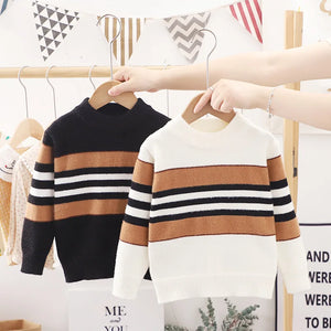 Two children's striped sweaters on hangers with a blurred background.