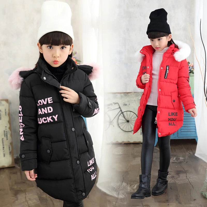 Two children wearing winter jackets with fur-lined hoods in a room.