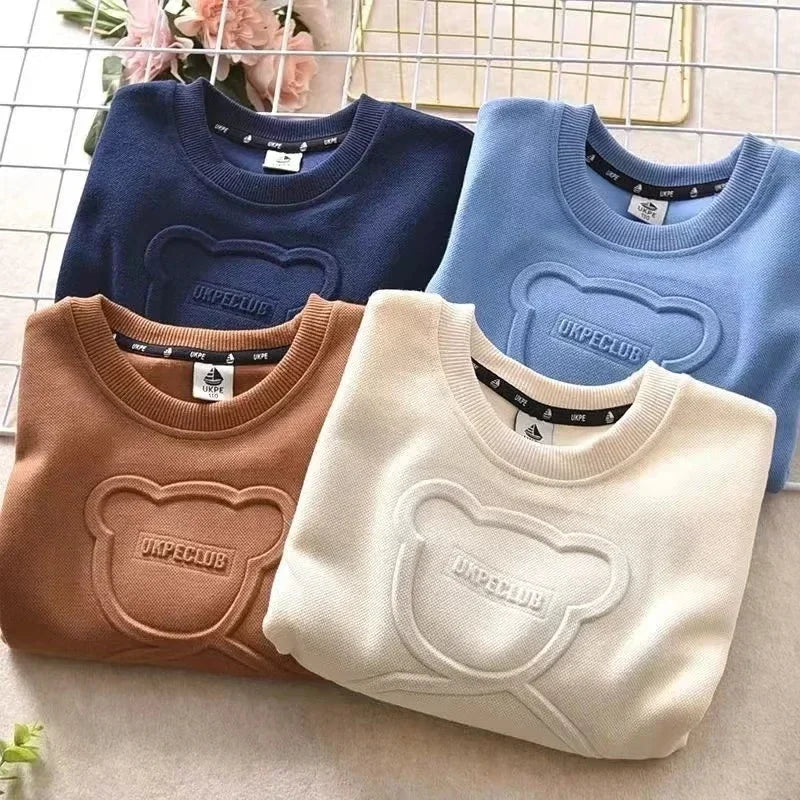 Four folded sweaters in blue, brown, and beige with a brand logo on a neutral background.