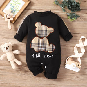 Black baby romper with plaid bear design and 'mini bear' text on a wooden surface with toys.